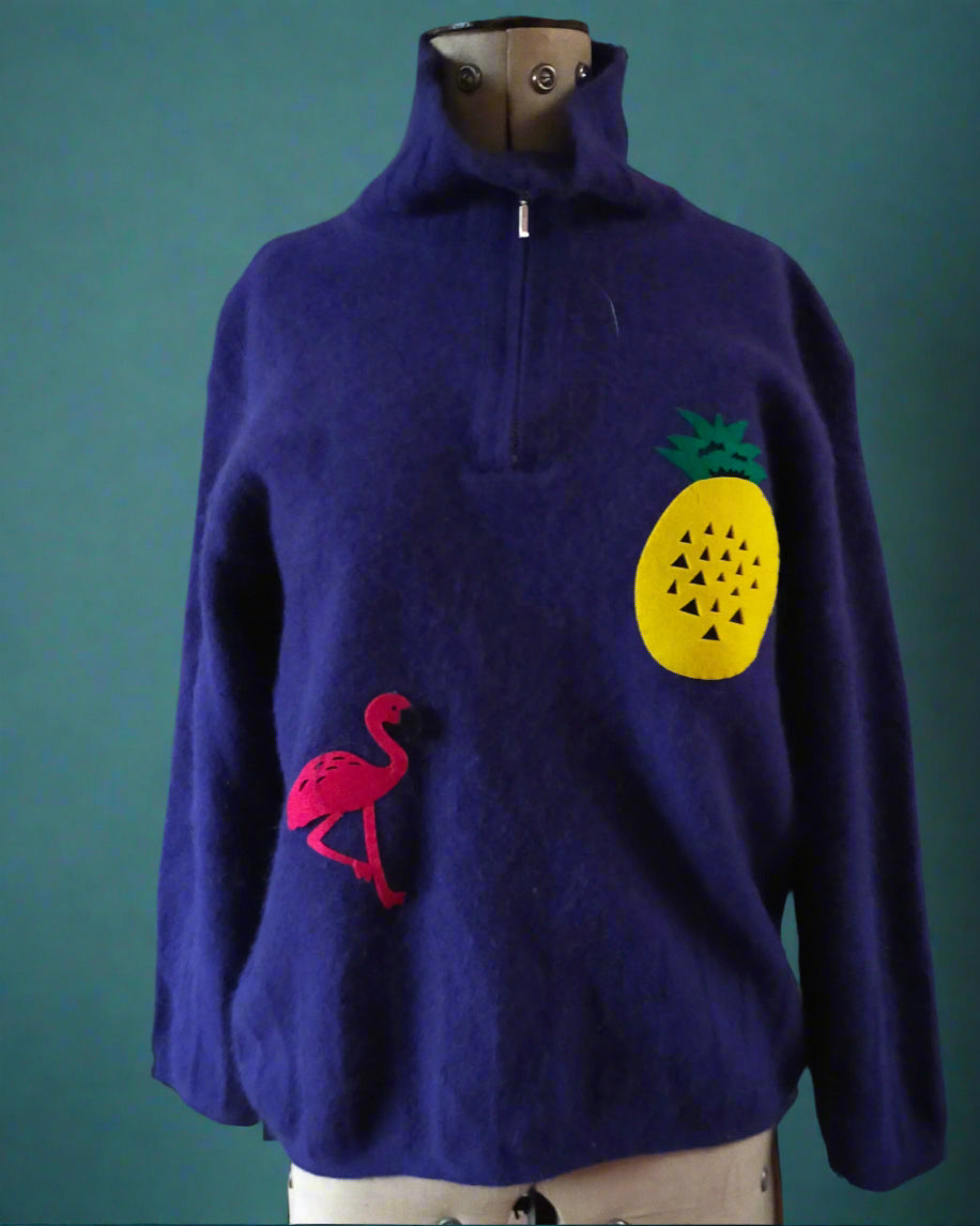 This is a royal blue lambswool sweater with a zip fastening. It is embellished with a pineapple and a flamingo