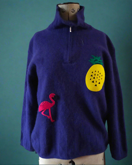 This is a royal blue lambswool sweater with a zip fastening. It is embellished with a pineapple and a flamingo