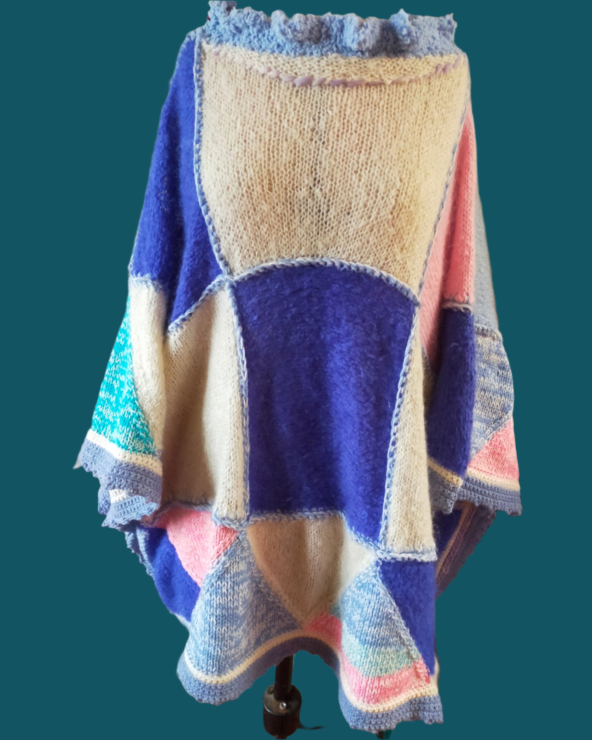 This is a long knitted poncho in cream, pink, light blue and dark blue. Made by not Your Nana in DUnedin, New Zealand