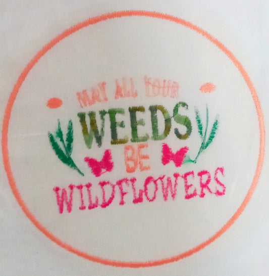 Embroidery  with text 'May all your weeds be wildflowers' on a white background