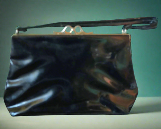 This is a black patent vinyl handbag with a strap and gold clasp. Found by Not Your Nana in Dunedin, New Zealand.