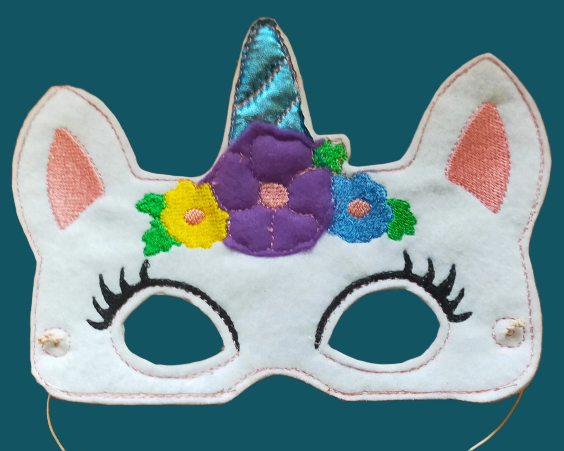 This white unicorn mask has a blue horn surrounded by flowers. Made by Not Your Nana in Dunedin. New Zealnd