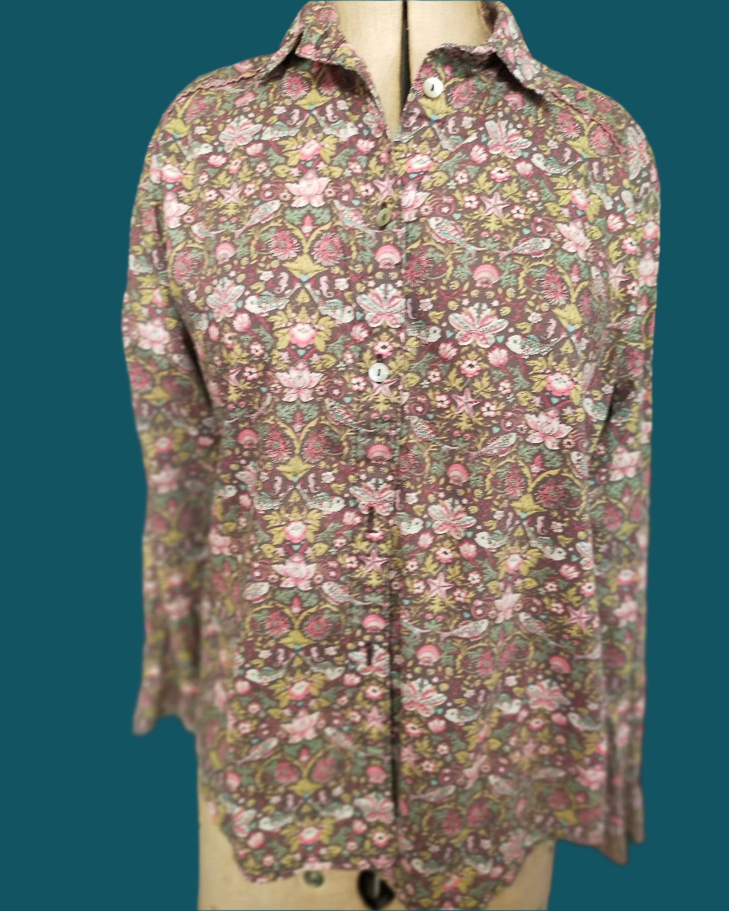 This is a classic styled shirt made from Liberty tana lawn. it is brownwith a ppretty floral pattern which includes a small fish. It features piped shoulder seams and shell buttons