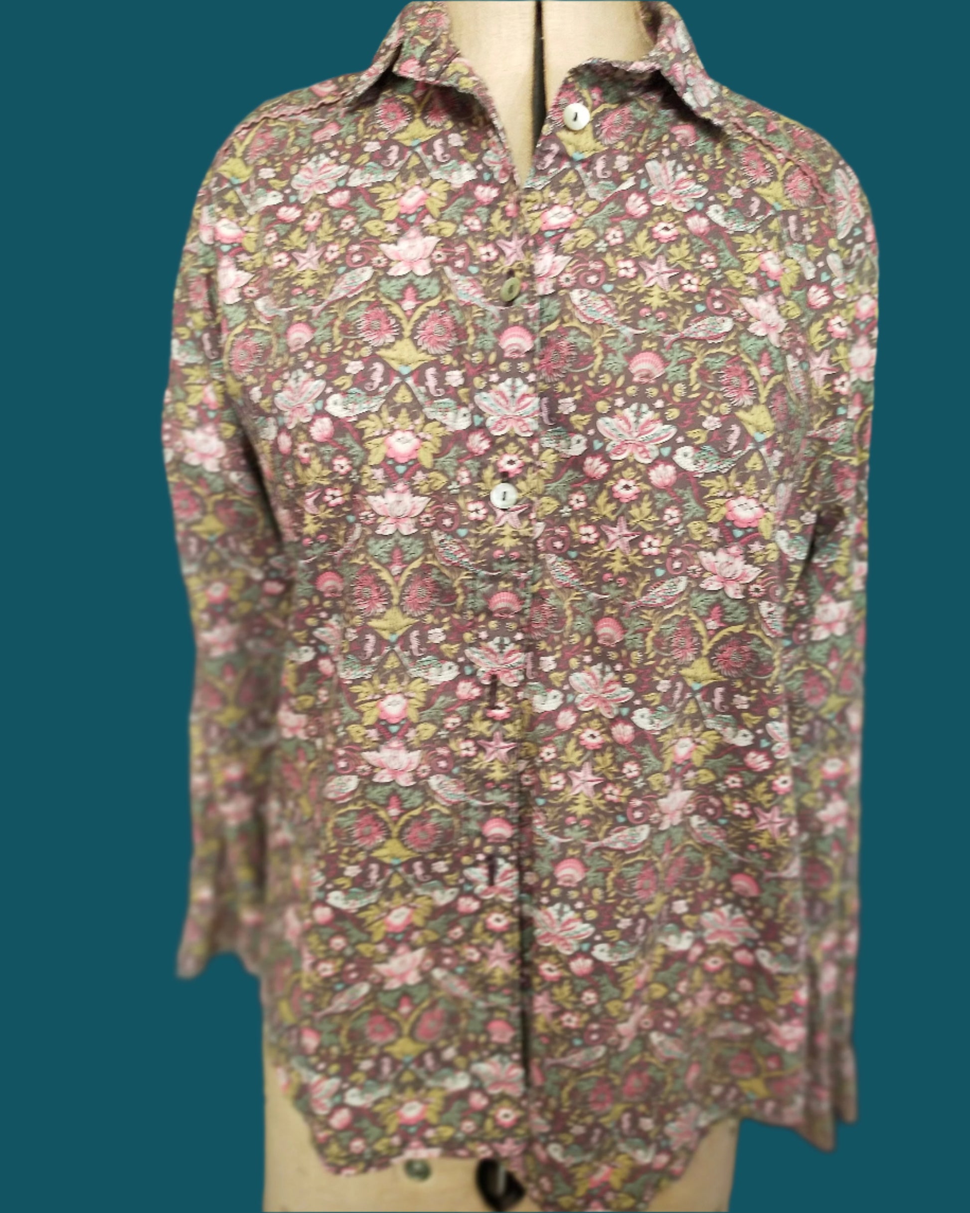 This is a classic styled shirt made from Liberty tana lawn. it is brownwith a ppretty floral pattern which includes a small fish. It features piped shoulder seams and shell buttons