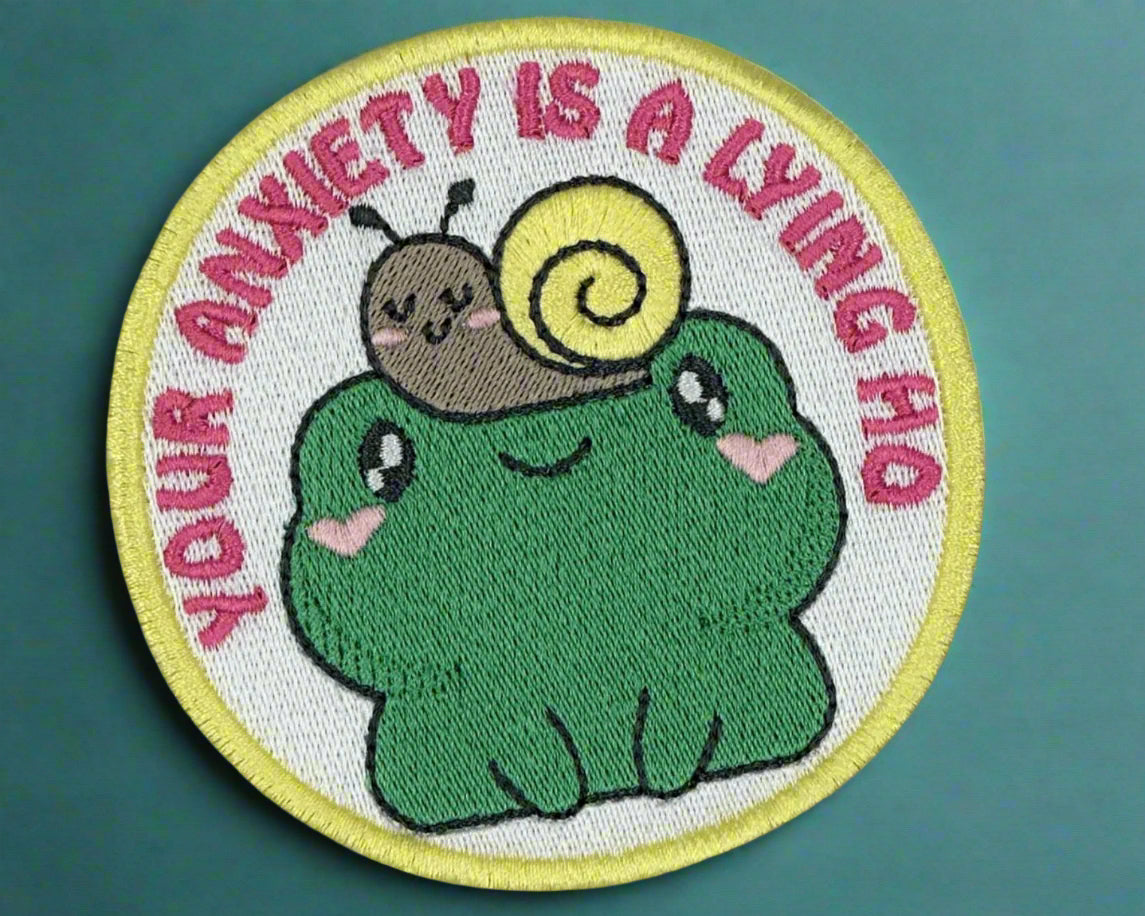 Circular patch with a cartoon frog and snail, text 'Your anxiety is a lying ho', made by Not our Nana, Dunedin, New Zealand