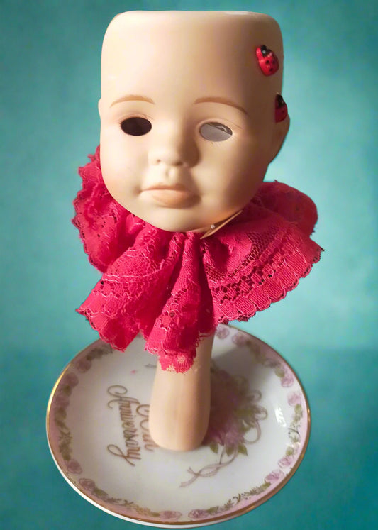 Doll head tealight with a red lace collar  and a ladybird on a decorative plate.  Made by Not You Nana in Dunedin, New Zealand