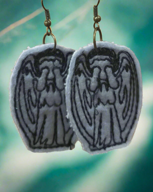 These are handmade grey felt earrings of the stone angels from Doctor Who. Made by Not Your Nana, Dunedin, New Zealand