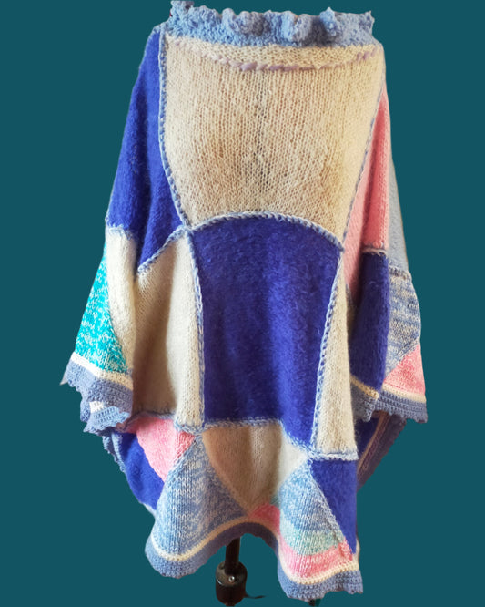 This is a long knitted poncho in cream, pink, light blue and dark blue. Made by not Your Nana in DUnedin, New Zealand