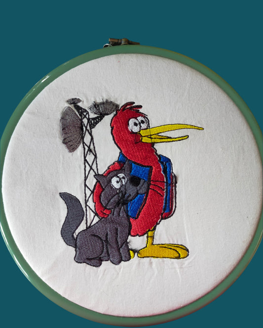 Kiwi is rust red and wears a blue waistcoat. Cat is grey. They are standing in front of a tv transmitter