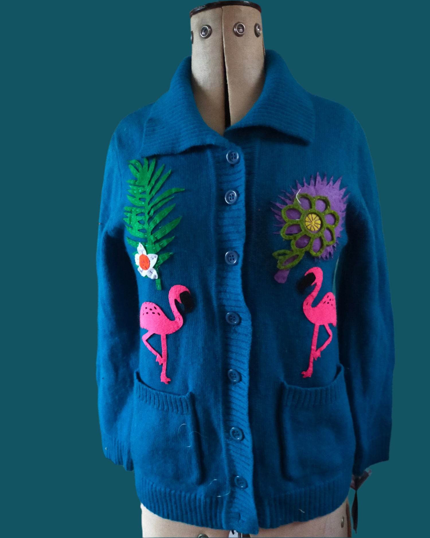 This is a peacock blue cardigan embellished with flower and flamingos. Made by not your nana in Dunedin New Zealand