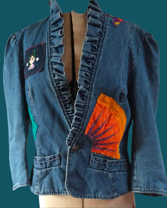 This blue denim jacket has a frilled denim collar, a small cartoon of Frida and an orange ray of sun on the front. The back consist of raw applique of Frida on ew silk and more raw applique. Made by Not Your Nana in Dunedin, New Zealand